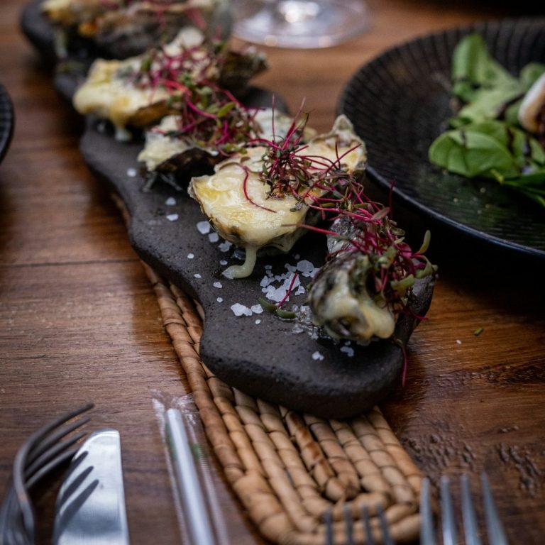 Des huîtres gratinées au foie gras sur une ardoise, accompagnées de verdure.