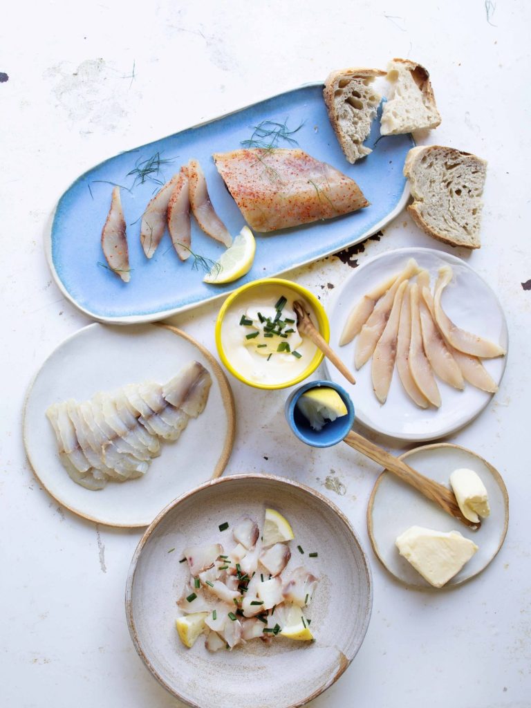 Assortiment de poissons crus, pain, citron et sauces sur des assiettes blanches et bleues.