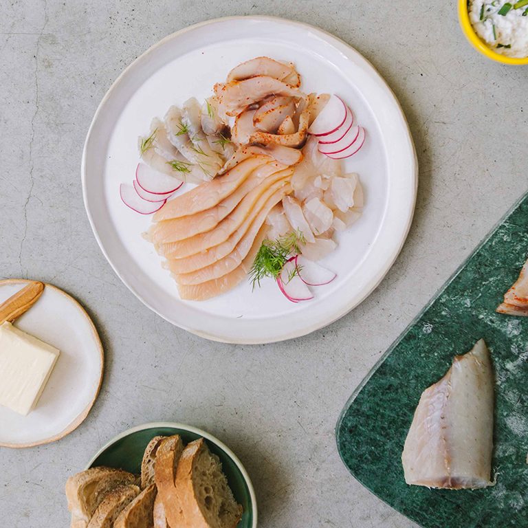 Assortiment de poissons fumés tranchés avec radis et pain sur une table.
