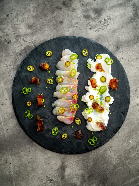 Filets de poisson garnis de légumes verts et croutons, présentés sur une ardoise noire.