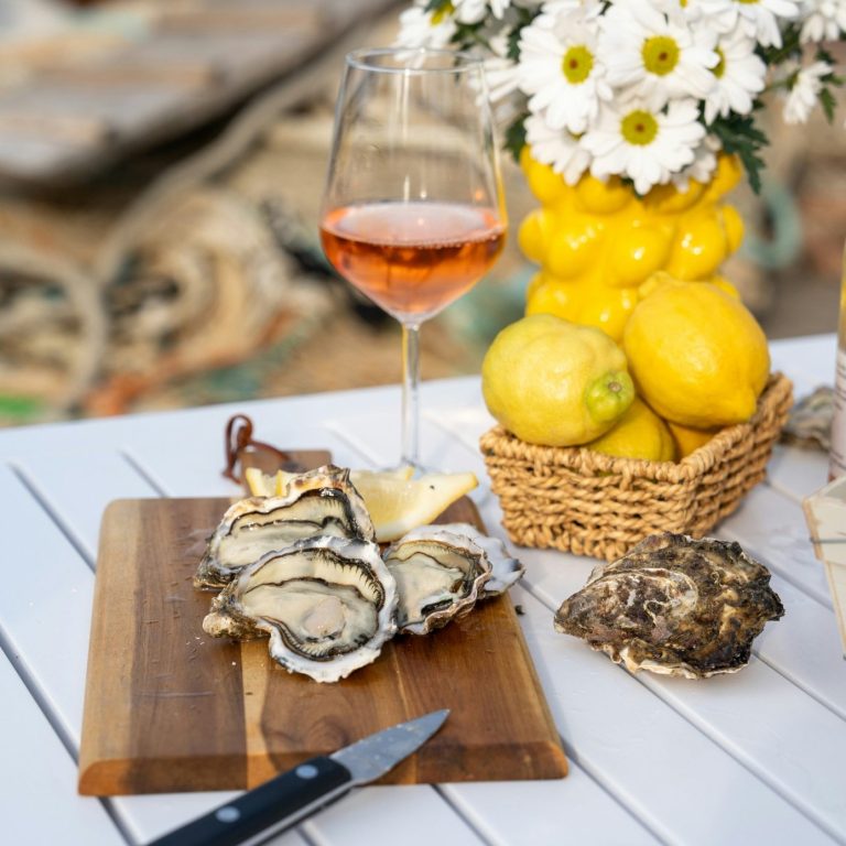 Plateau d'huîtres avec un verre de rosé et des citrons sur une table en extérieur.