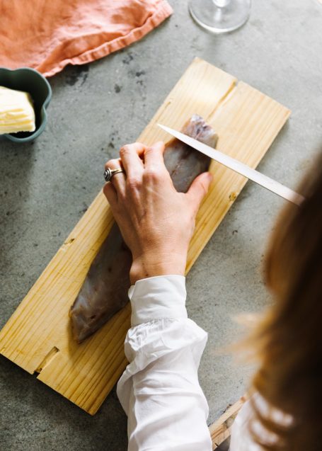Main d'une personne coupant un filet de mulet sur une planche en bois.