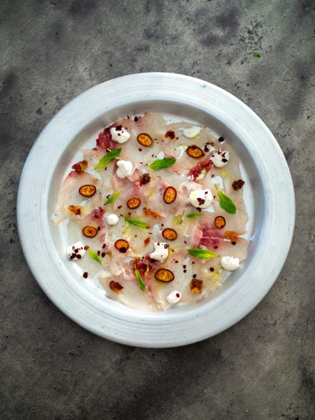 Plat de sashimi avec poissons, fleurs comestibles et crème, décoré de graines.