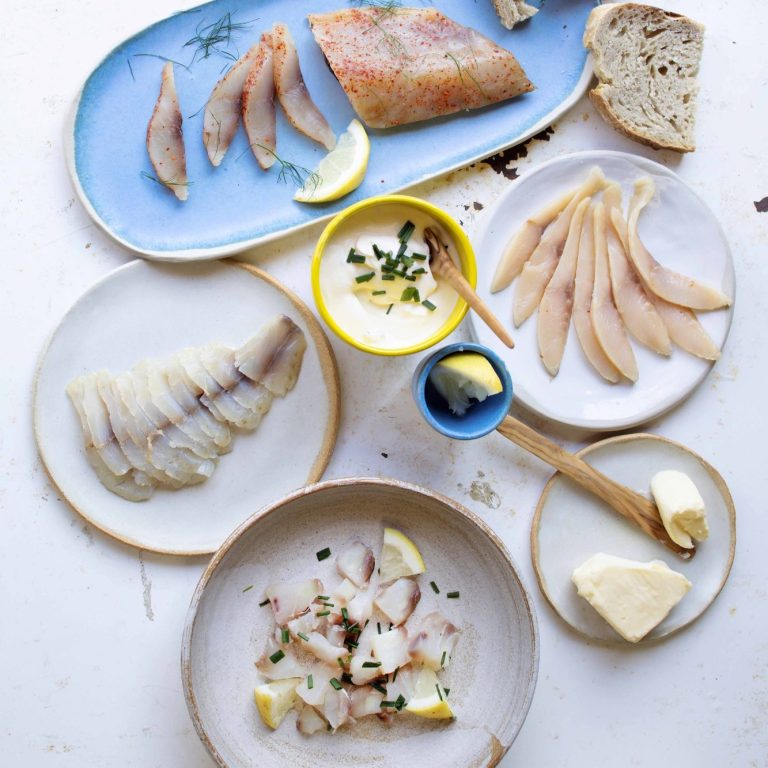 Assortiment de poisson, morceaux de pain, citron et sauces, présenté sur des assiettes.