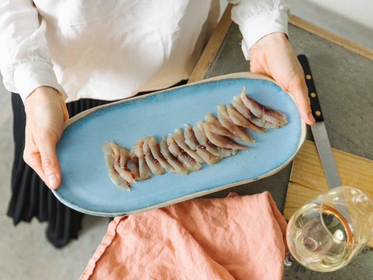 Assiette bleue tenue par des mains, contenant des tranches fines de poisson fumé.