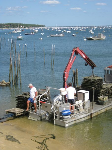 Deux personnes travaillent sur une barge, avec des équipements, près de l'eau et des bateaux.
