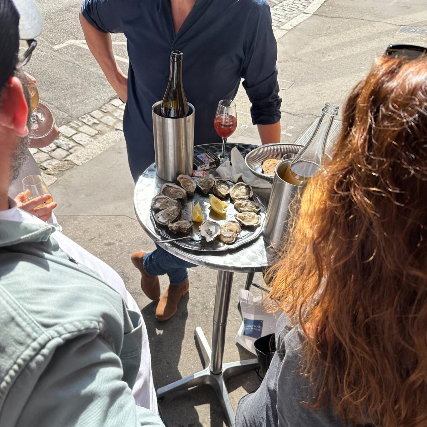 Clients avec plateau d'huîtres et verres de vin sur une terrasse.