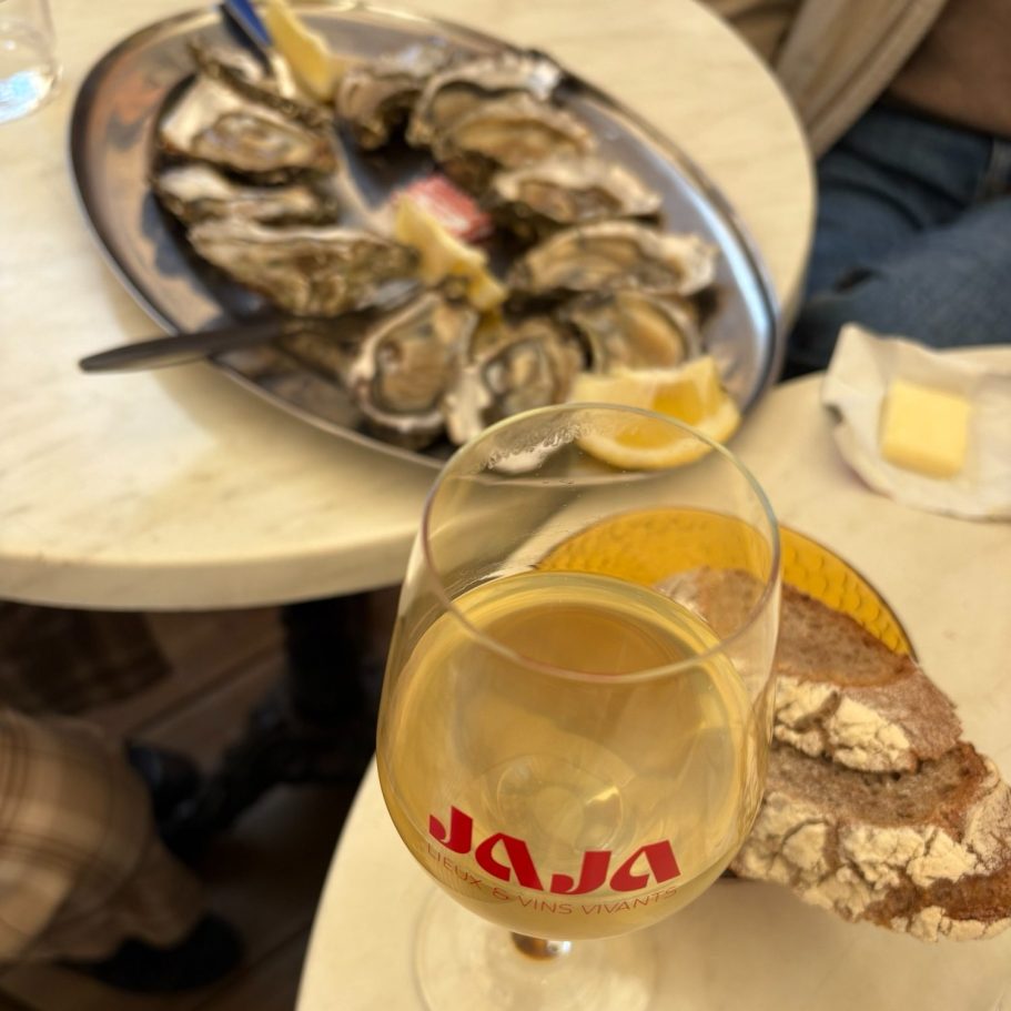 Assiette d'huîtres avec un verre de vin blanc et du pain sur une table.